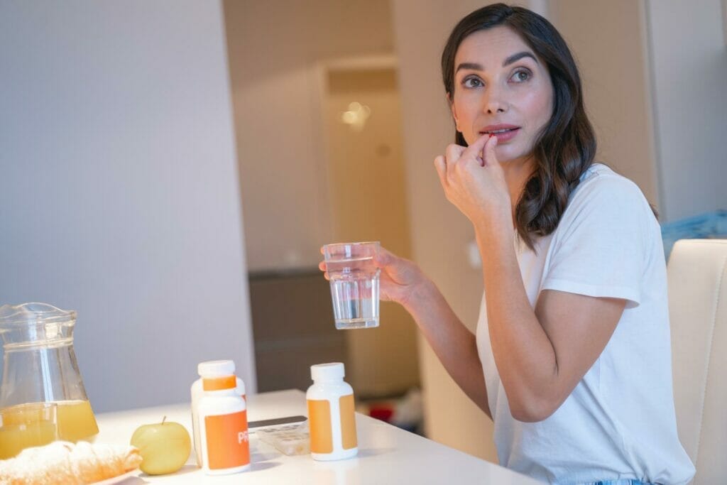 How Much Water Should You Drink With Vitamins? image of a woman with a glass of water taking vitamins